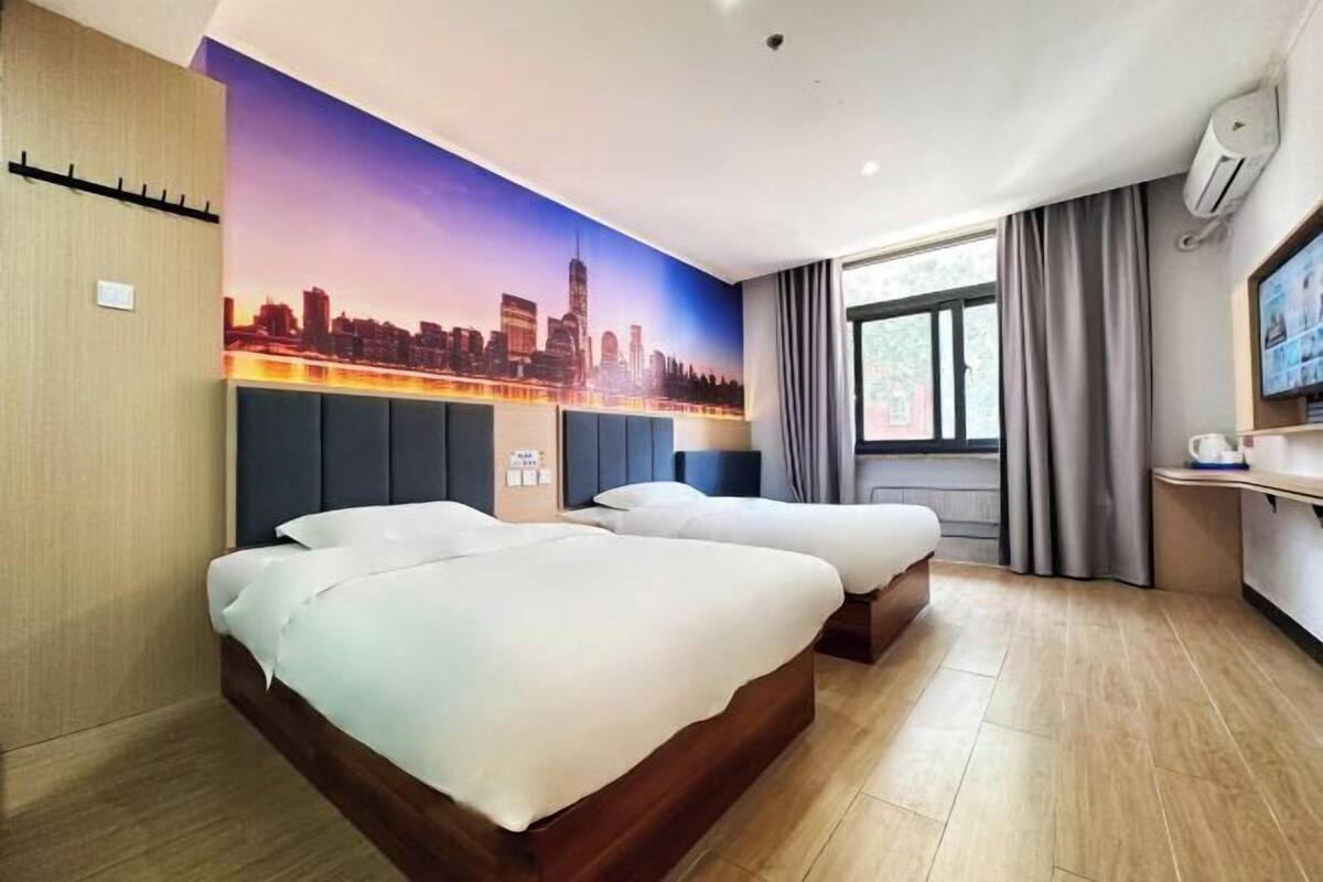 Een hotelkamer met twee bedden, een muurschildering van een stadsgezicht, een raam met gordijnen en een televisie aan de muur.