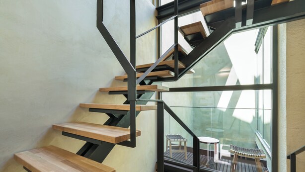 Una moderna scala con gradini in legno e ringhiere in metallo, che conduce a un balcone con mobili da esterno.