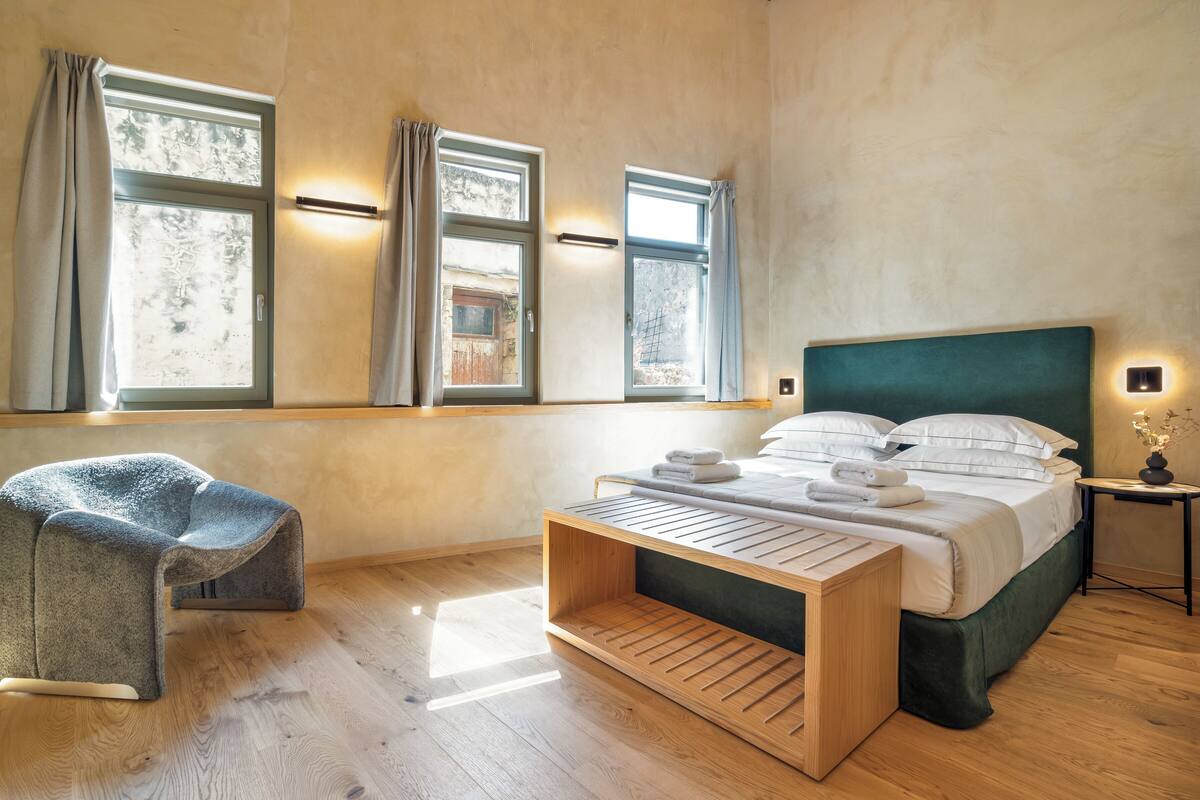 A modern bedroom with a bed, a wooden bedside table, a chair, and a window with curtains.