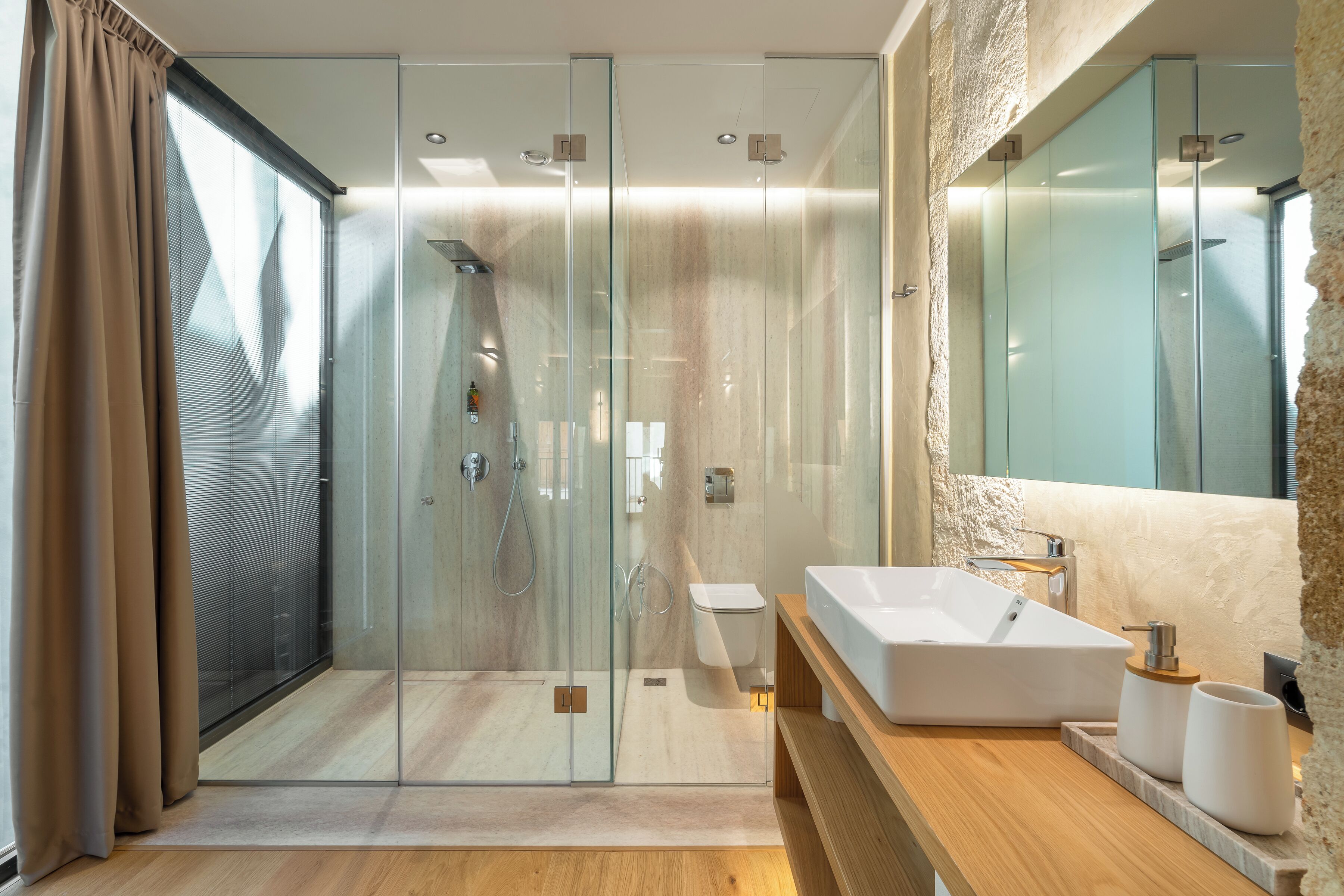 A modern bathroom with a glass-enclosed shower, a large mirror, and a wooden vanity with a white sink.