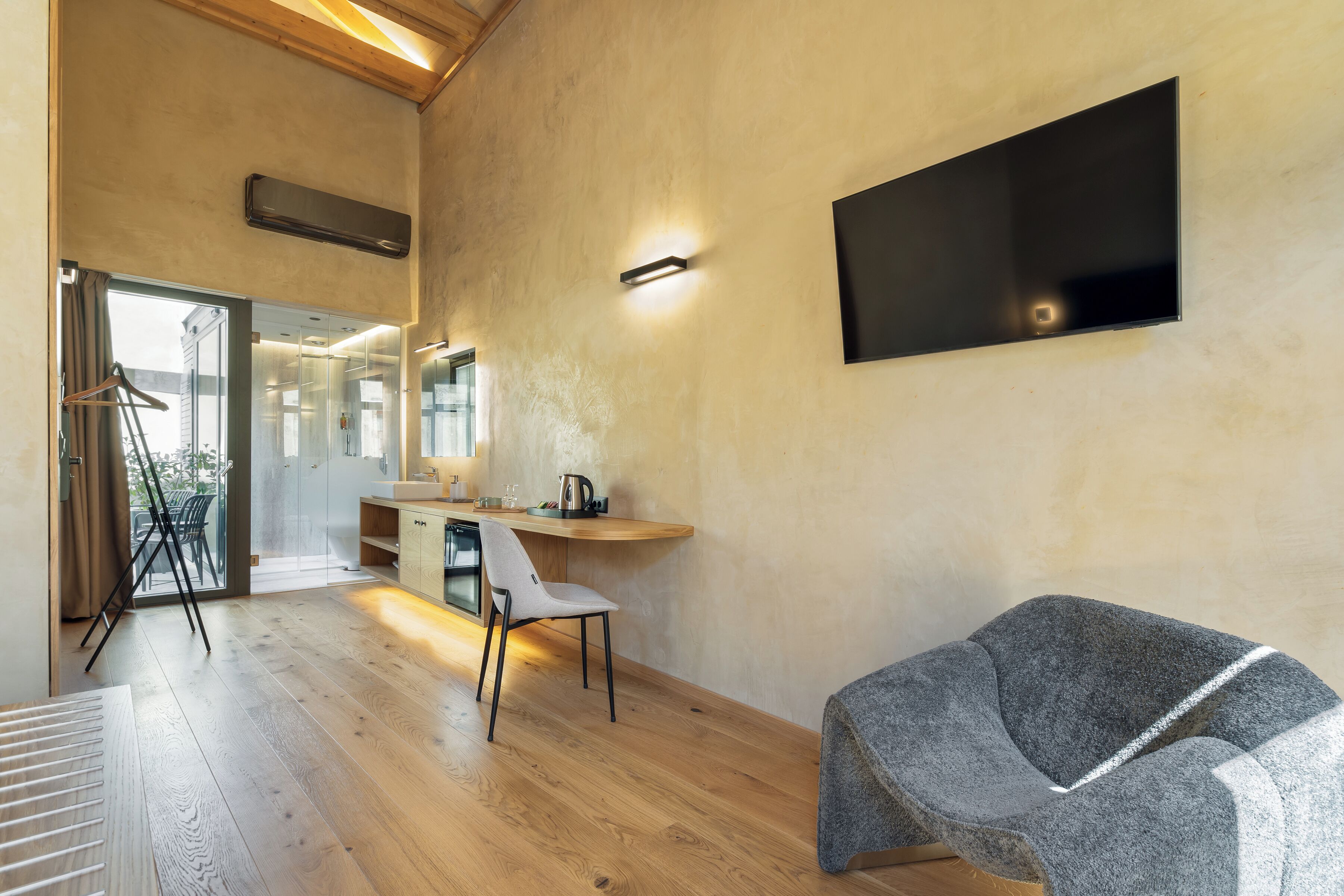 Une chambre moderne avec un plancher en bois, un bureau avec une chaise, un téléviseur fixé au mur et une grande fenêtre.