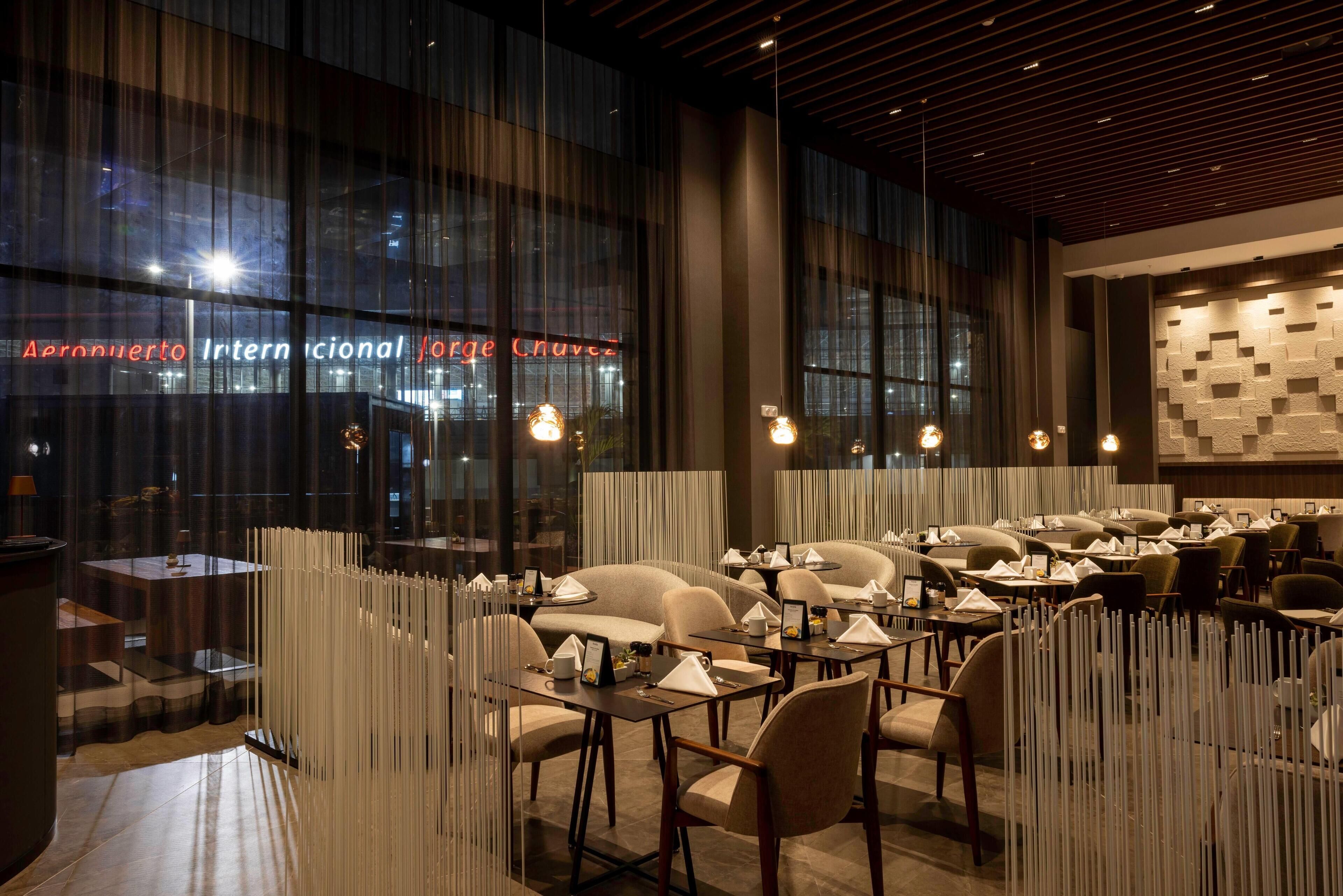 A modern restaurant with a view of the exterior through large windows, featuring a sign that reads "Parrónuevo Internacional Jorge Chavez".