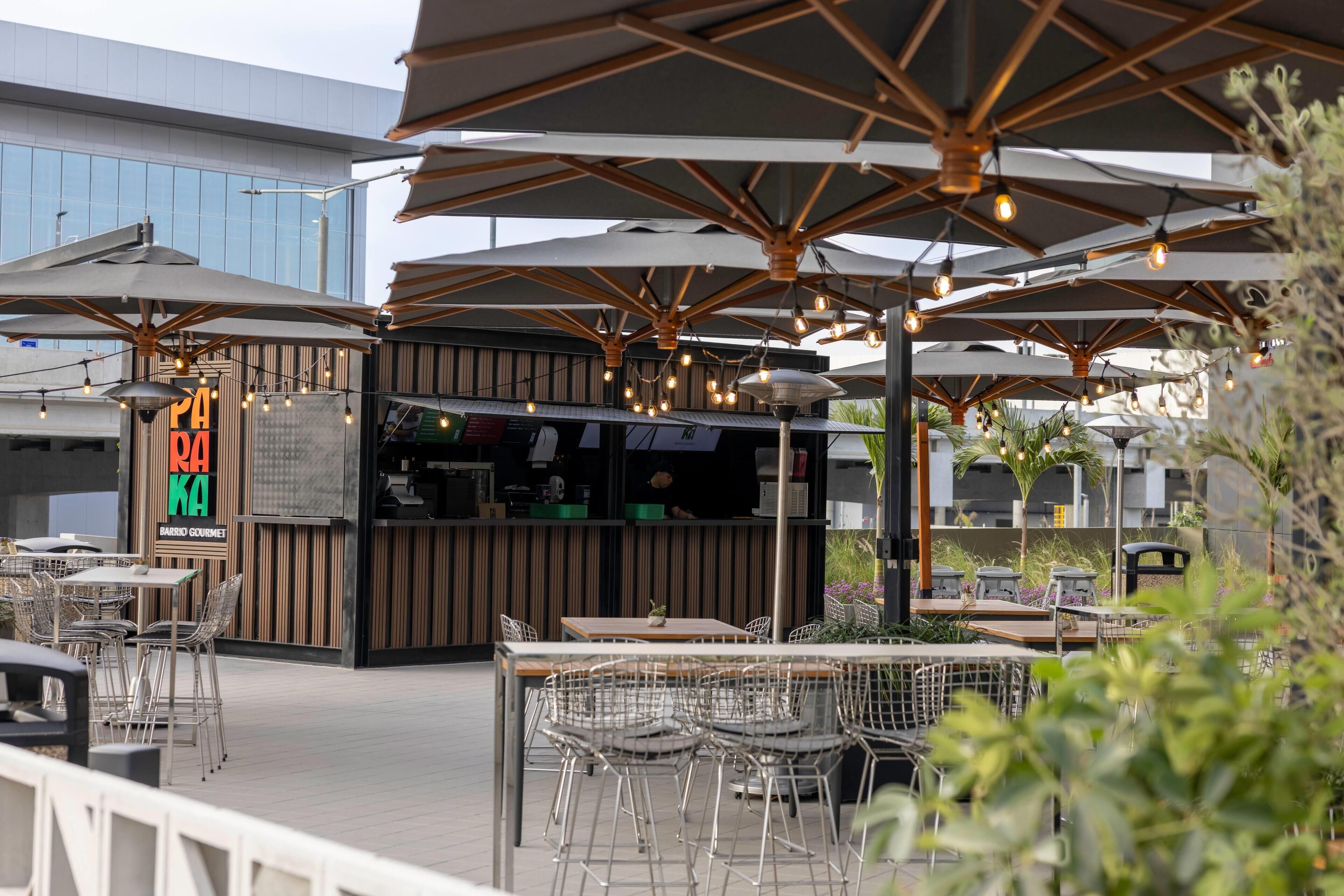 An outdoor dining area with multiple tables and chairs, umbrellas, and string lights.