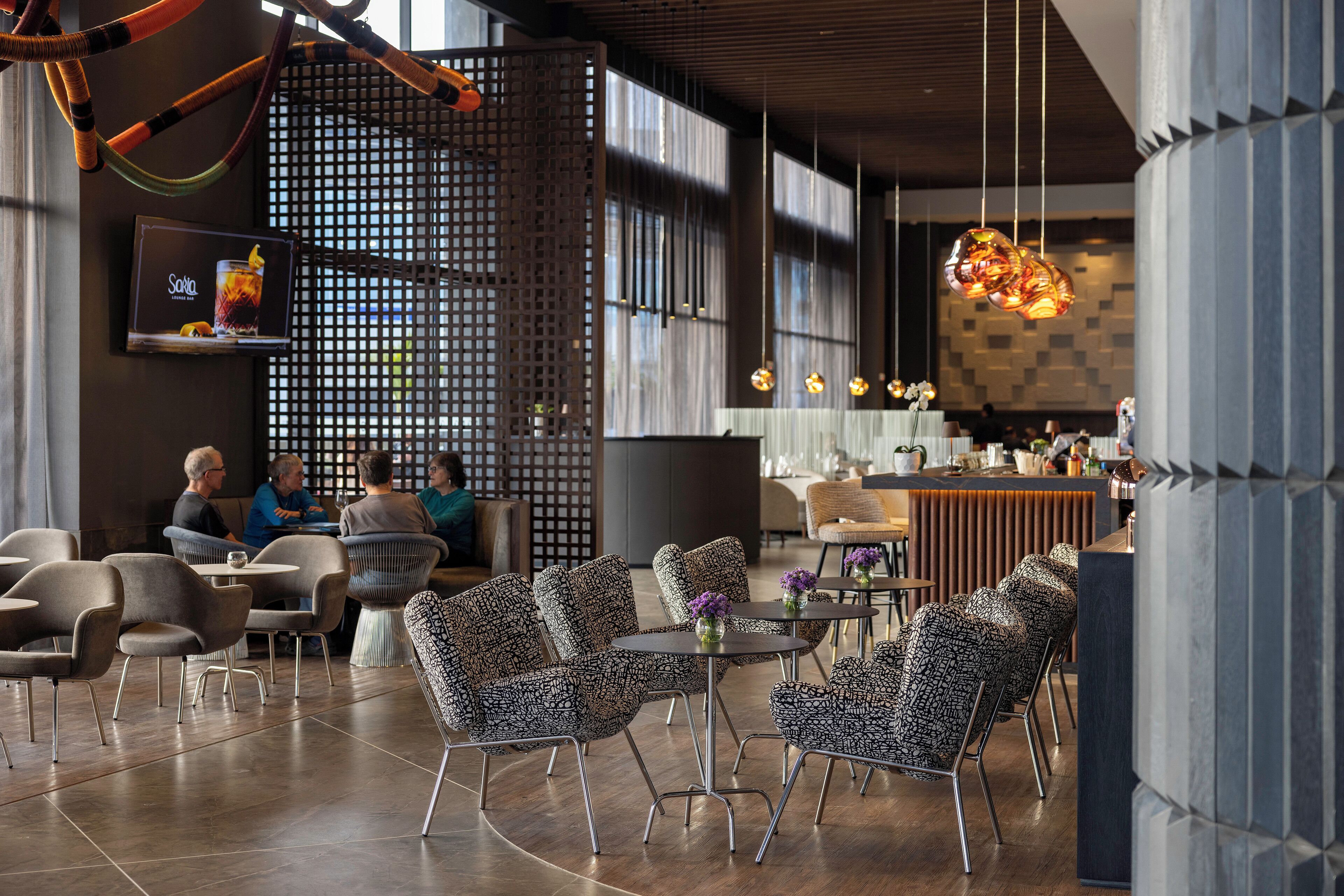 A modern interior with patterned chairs, a bar area, and a seating area with people.