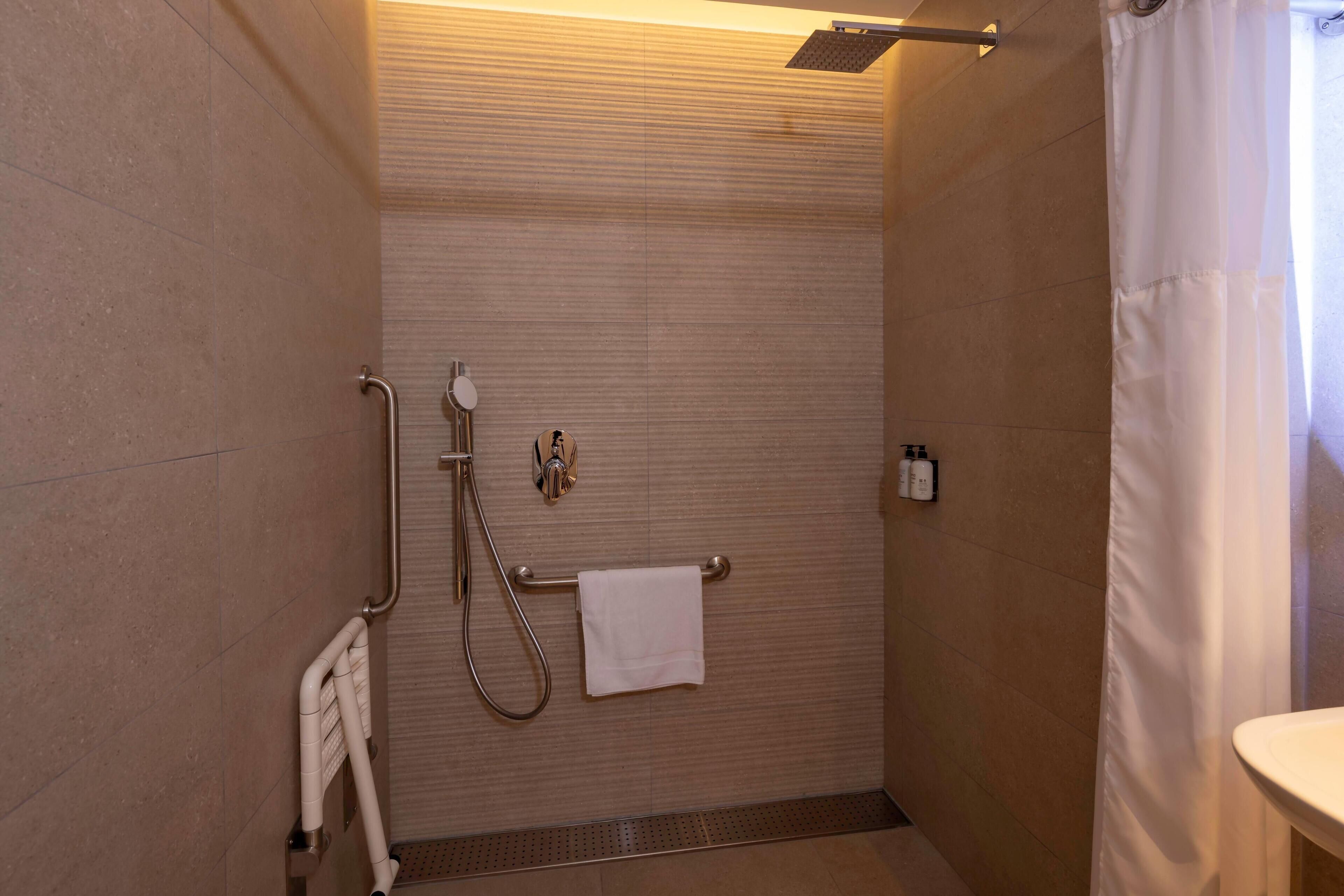 Un bagno moderno con doccia, maniglie di sostegno, porta asciugamani e water.