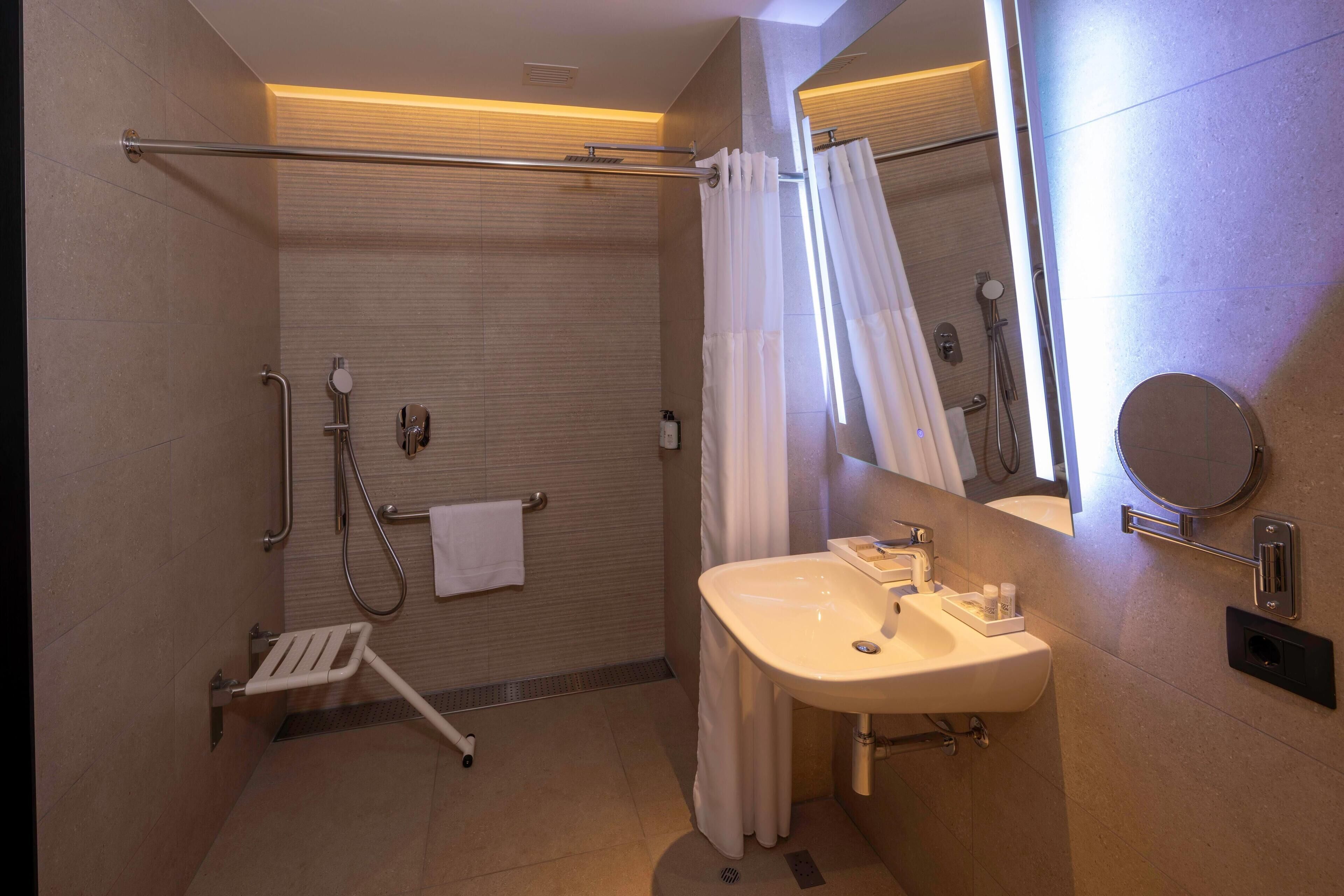 A modern bathroom with a walk-in shower, grab bars, a white sink, and a large mirror.