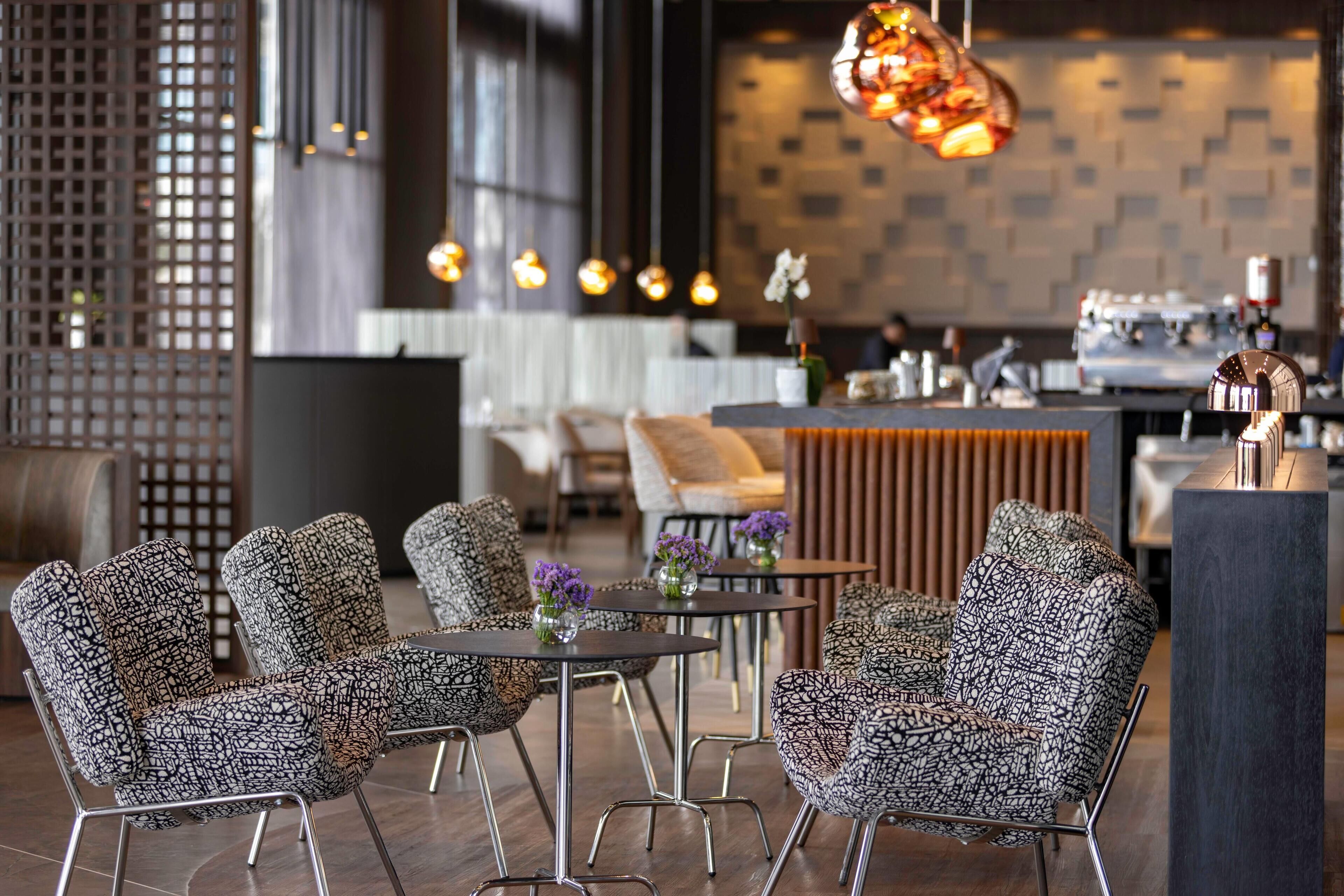 A modern interior with patterned chairs, round tables, and hanging pendant lights.