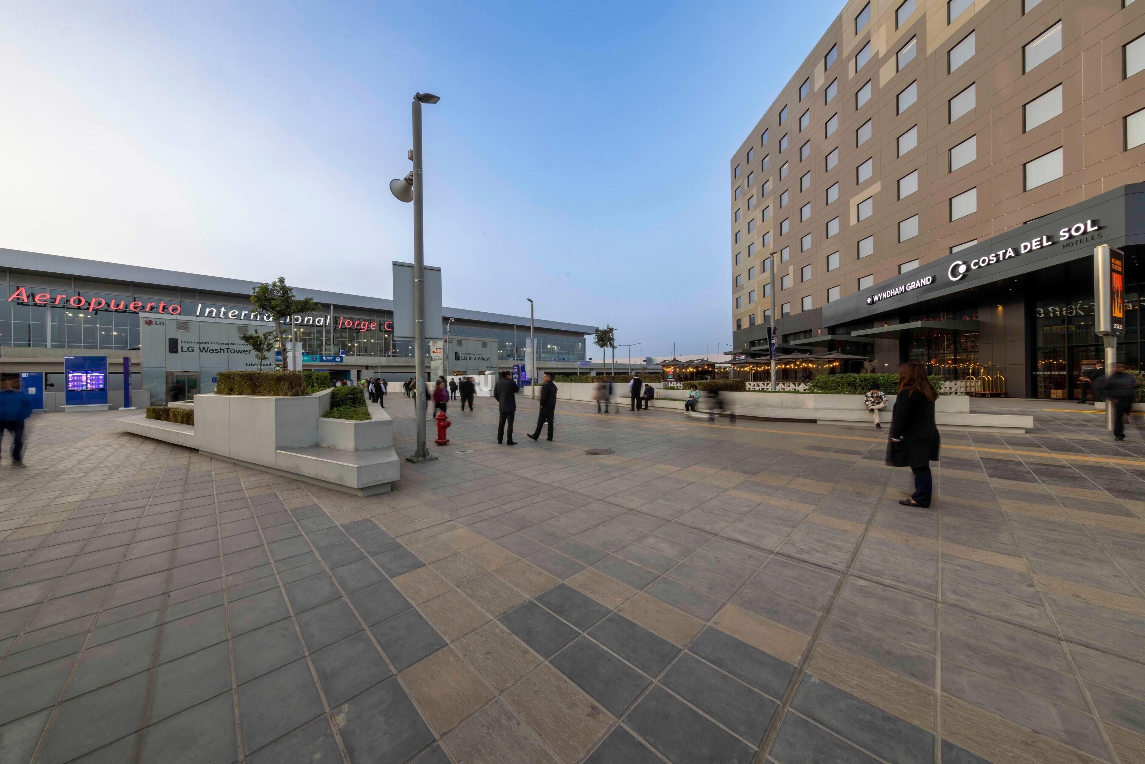 Una plaza urbana con un edificio moderno que muestra un letrero de 'Wyndham Grand Hotels'.