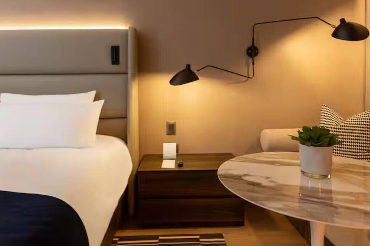 Une chambre d’hôtel avec un lit, une table de chevet, une lampe et une petite table sur laquelle est posée une plante.