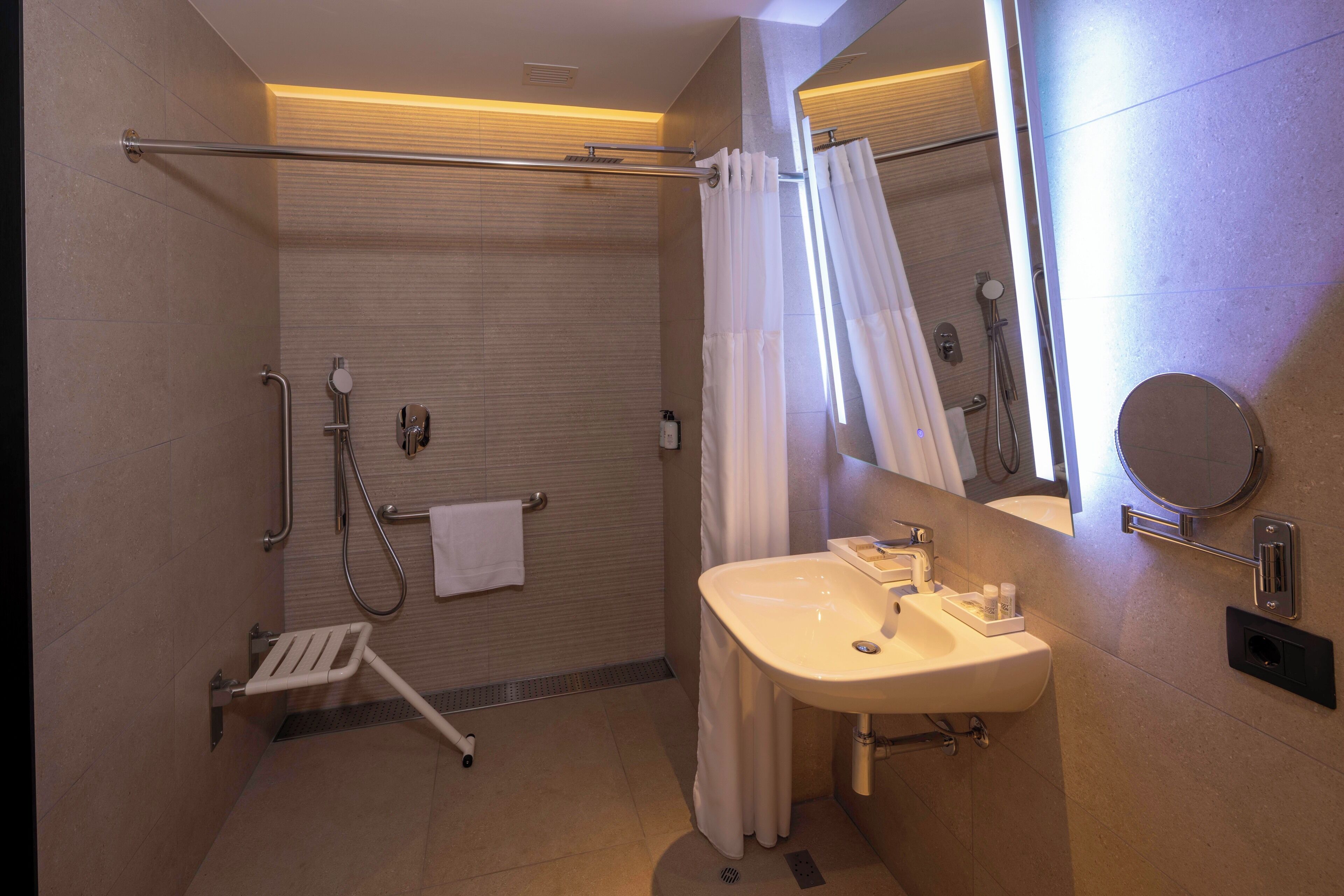 Een moderne badkamer met een douche, een handgreep en een wastafel met spiegel.