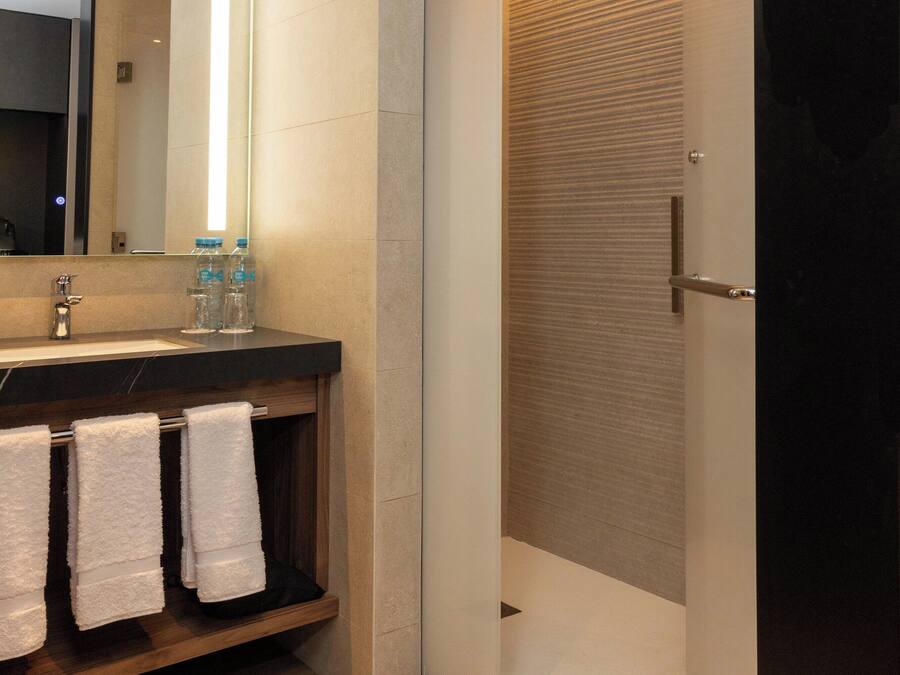 Un baño moderno con tocador de madera, un espejo grande y una ducha a ras de suelo.