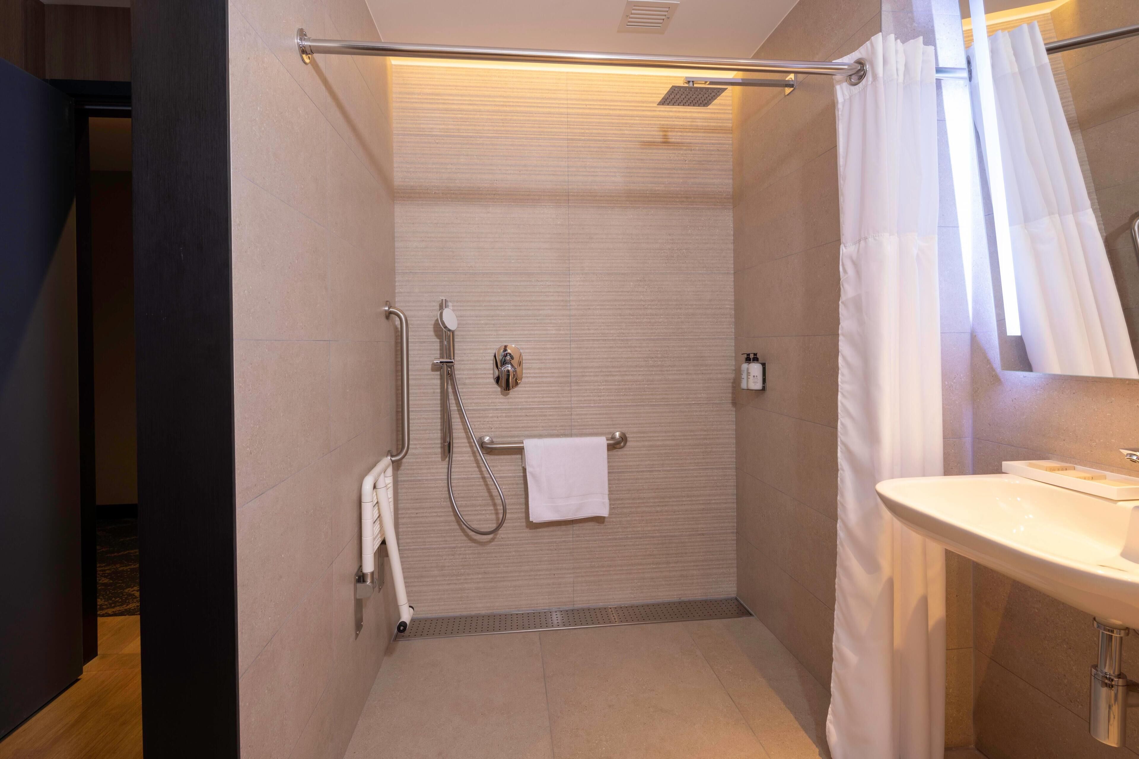A modern bathroom with a shower, a towel rack, a sink, and a mirror.