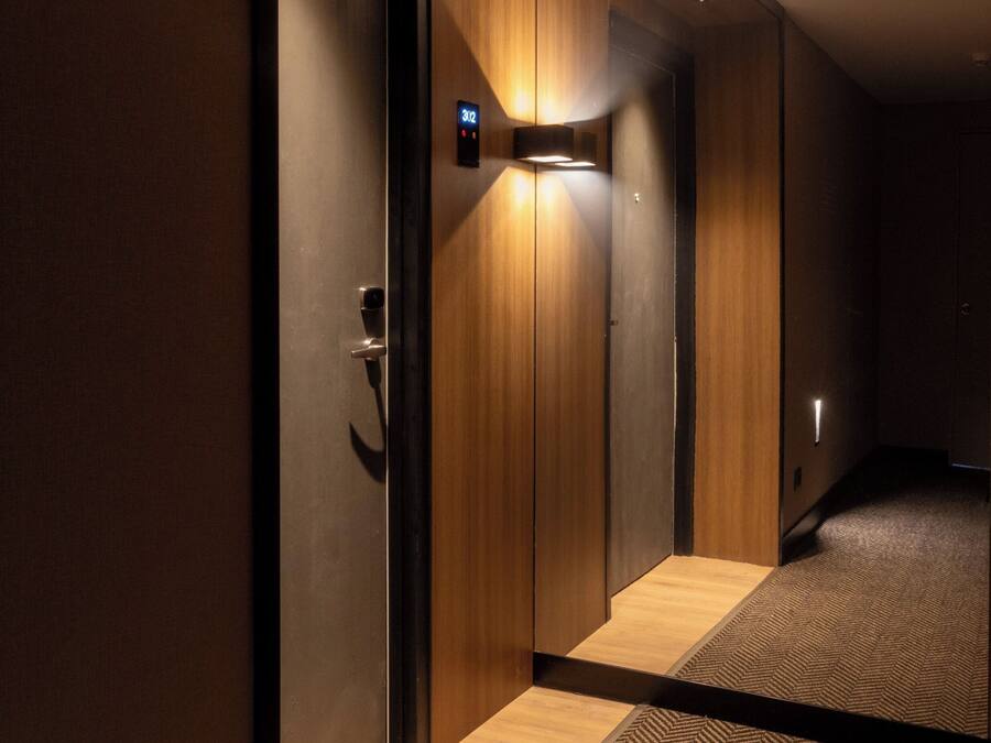 Un pasillo moderno de hotel con paneles de madera, un reloj digital y suelo alfombrado.
