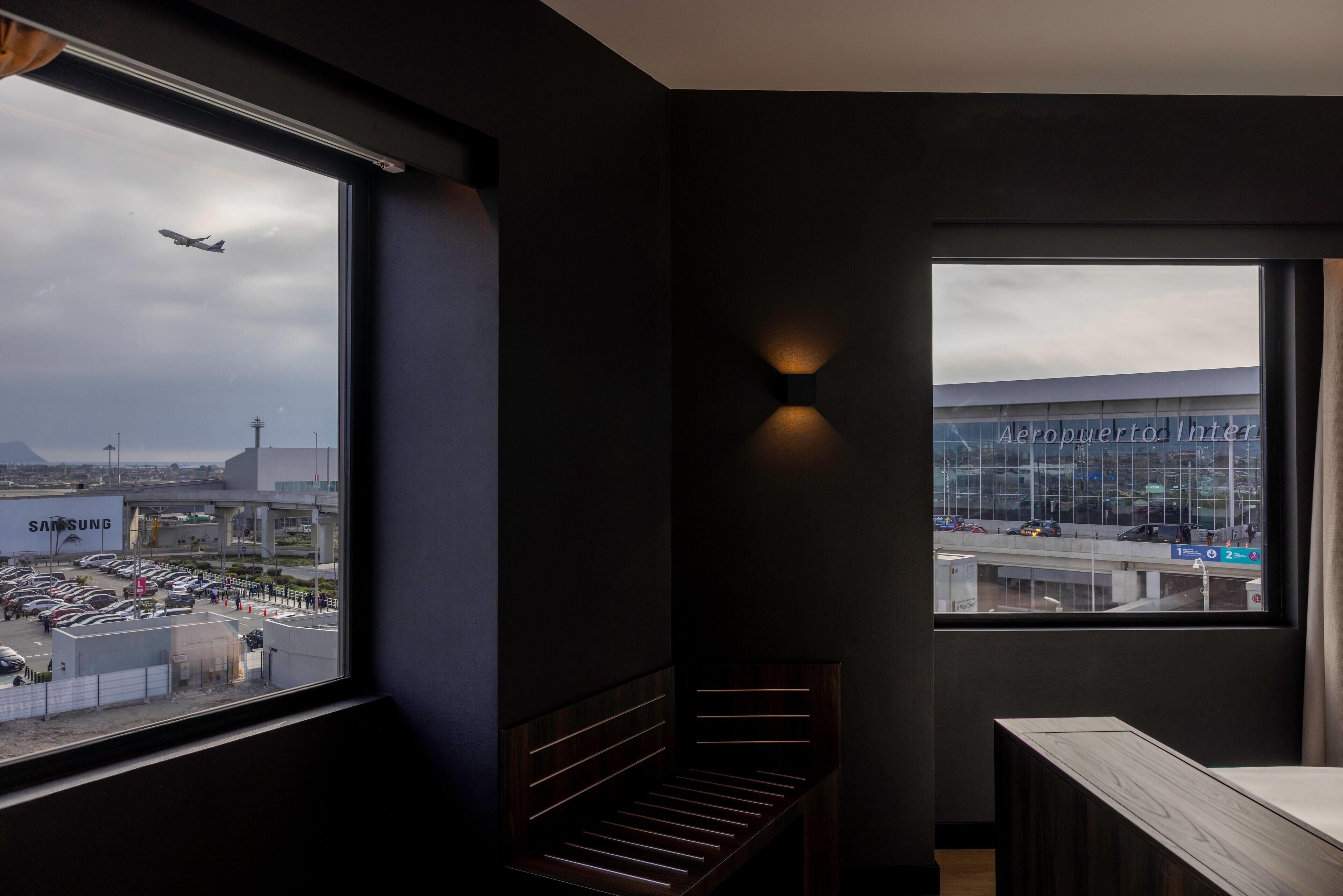 A hotel room with a large window offering a view of an airport and a building with a sign.