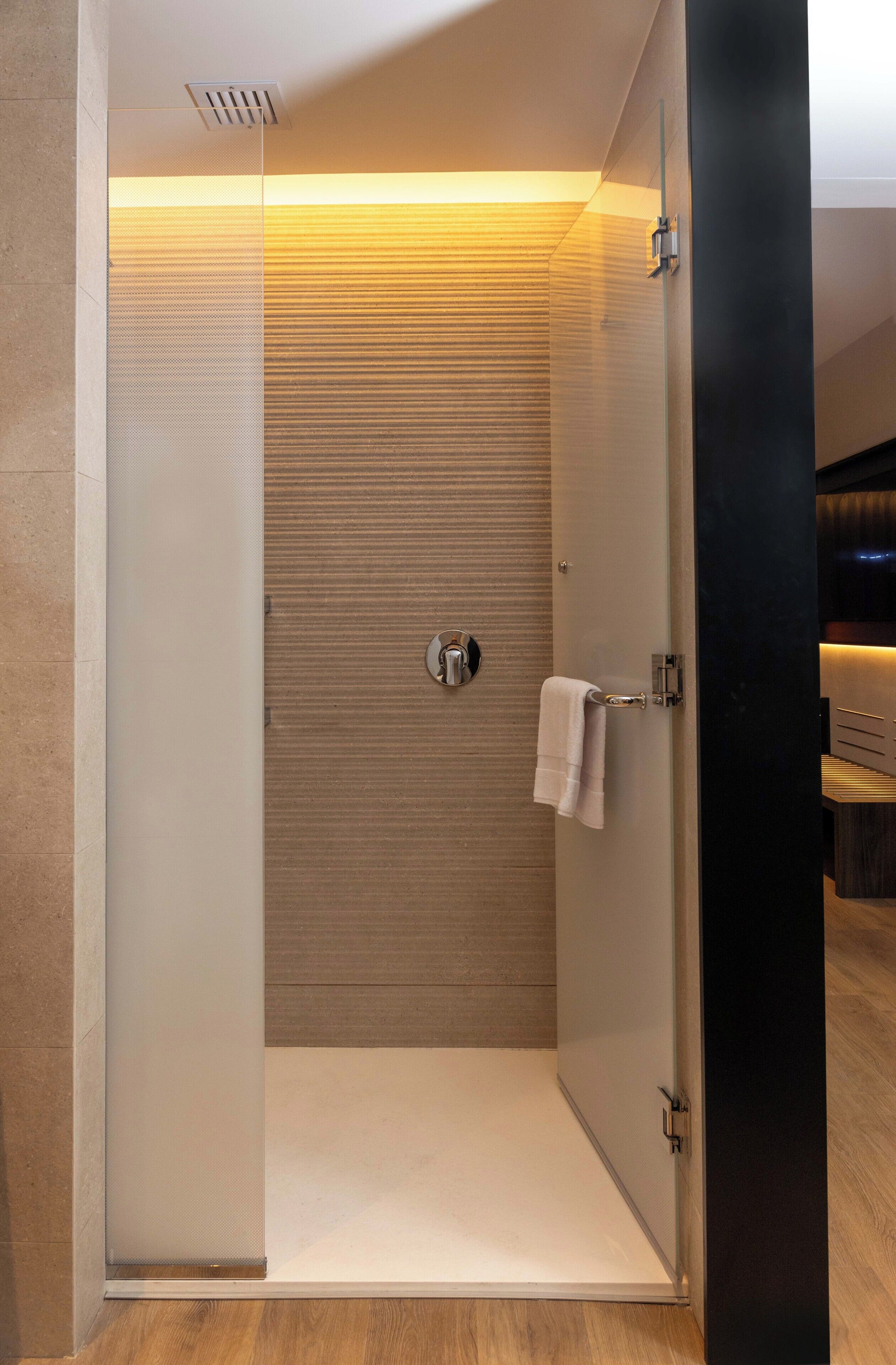 Un área de ducha moderna con puerta de cristal, una toalla colgada en la puerta y suelo de madera.