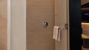 Un área de ducha moderna con puerta de cristal, una toalla colgada en la puerta y suelo de madera.