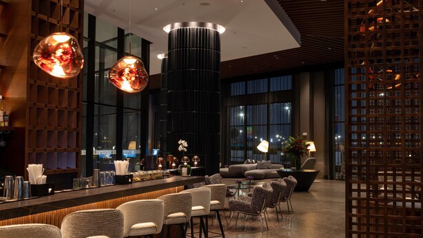 Un área de bar moderna con una barra alargada, varios taburetes y una columna decorativa central.