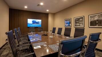 Un salón de conferencias con una gran mesa, sillas, una pantalla de televisión y cuadros en la pared.