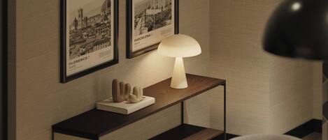 A room with a wooden console table displaying framed pictures of Florence and Barcelona, a white lamp, and a black floor lamp.