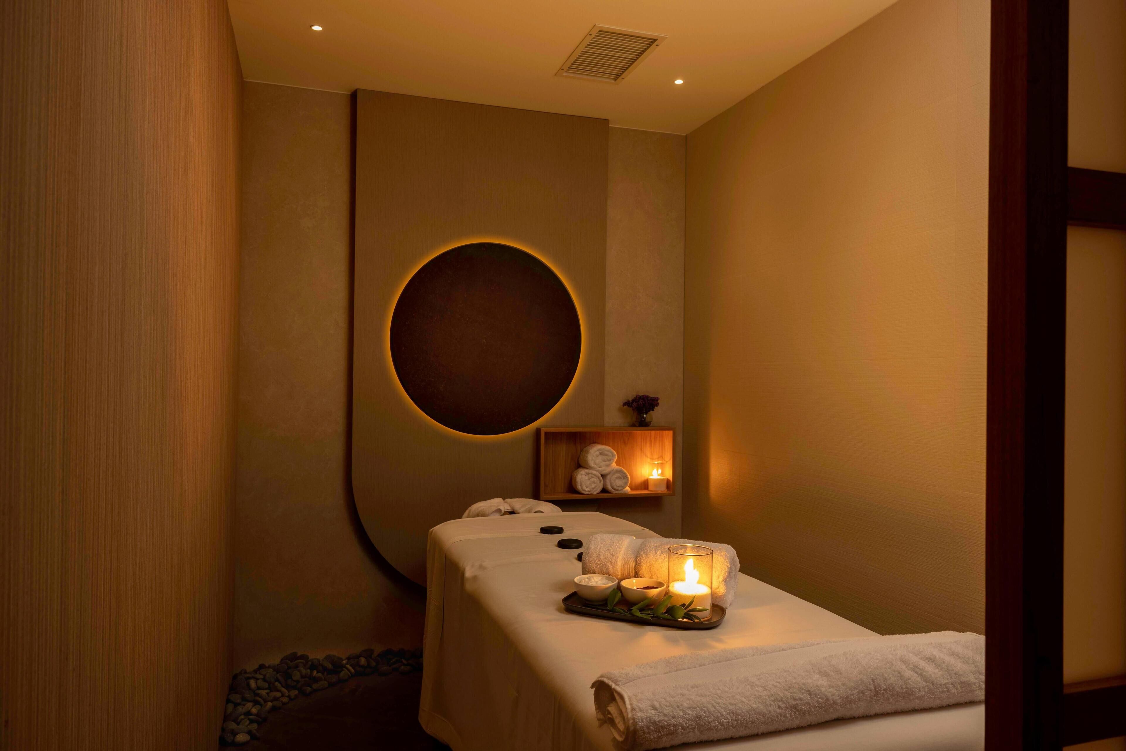 A spa room with a massage table, candles, and a circular wall feature.