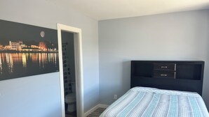 Un dormitorio con cama, mesita de noche, televisor montado en la pared y baño con inodoro y cortina de ducha.
