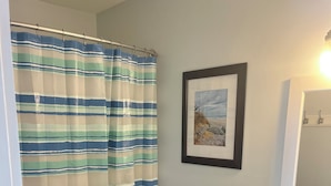 Un baño con cortina de ducha a rayas, un inodoro, un lavabo con encimera de granito, armarios de madera oscura y un cuadro en la pared.