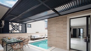 En modern uteplats med en pool, en matplats med stolar och ett bord samt en glasdörr som leder in till ett inomhusutrymme.