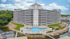 Un grande hotel a più piani con un cortile centrale che include una piscina, immerso nell'acqua e nel verde.
