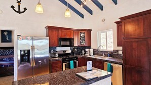 Cocina con encimeras de granito, electrodomésticos de acero inoxidable, armarios de madera y una lámpara colgante.