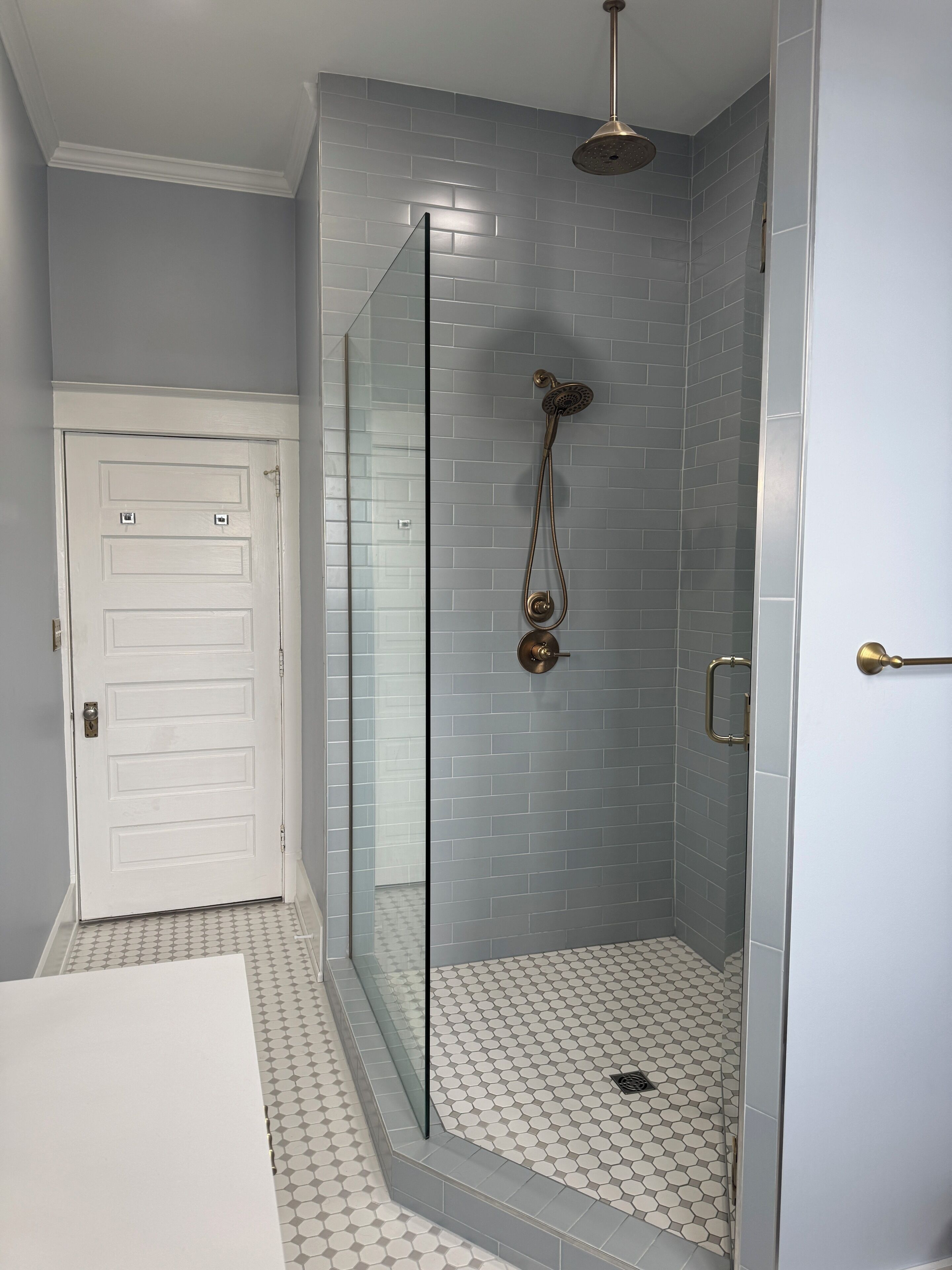 A bathroom with a glass-enclosed shower, a white door, and a patterned floor.