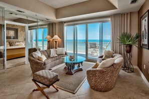 A spacious living area with a large glass door leading to a balcony with a view of the ocean. There are two patterned sofas, a coffee table, and a side table with a plant. - Empress 803 (Miramar Beach)