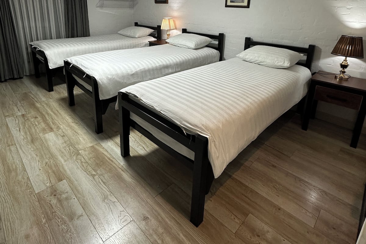 A hotel room with two single beds, wooden flooring, white walls, and a ceiling light.