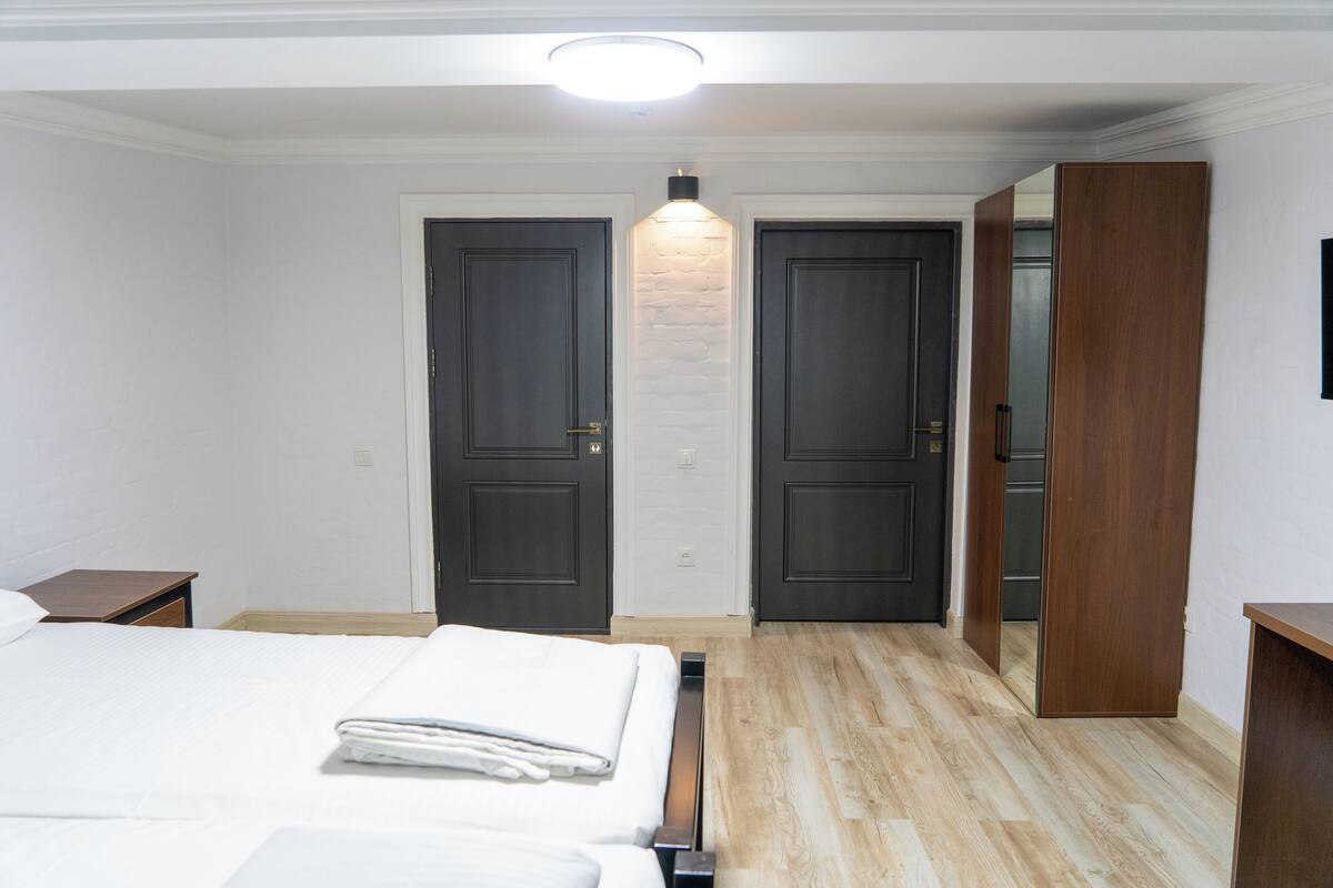 A hotel room with a bed, a nightstand, a wooden wardrobe, and a mirror.