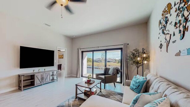A modern living room with a flat-screen TV, a sofa, a coffee table, and a large window offering a view of the outdoors.