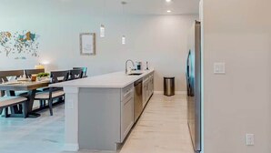 A modern kitchen with a central island, a dining area with a table and chairs, and a small trash bin.