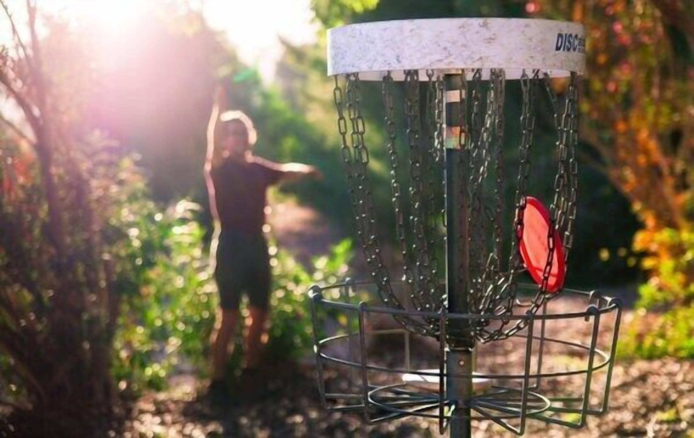 Un cesto de disc golf con cadenas y un disco rojo, situado en un entorno natural al aire libre.