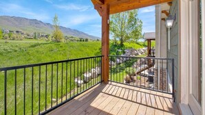 Eine Holzterrasse mit Metallgeländer, die auf eine Wiese und Berge blickt.