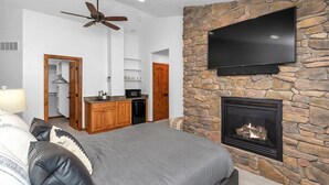 Ein modernes Schlafzimmer mit einer Wand aus Stein, einem Kamin, einem Flachbildfernseher und einem Deckenventilator.
