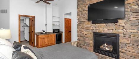 Une chambre moderne avec un mur d’accent en pierre, une cheminée, un téléviseur à écran plat et un ventilateur de plafond.