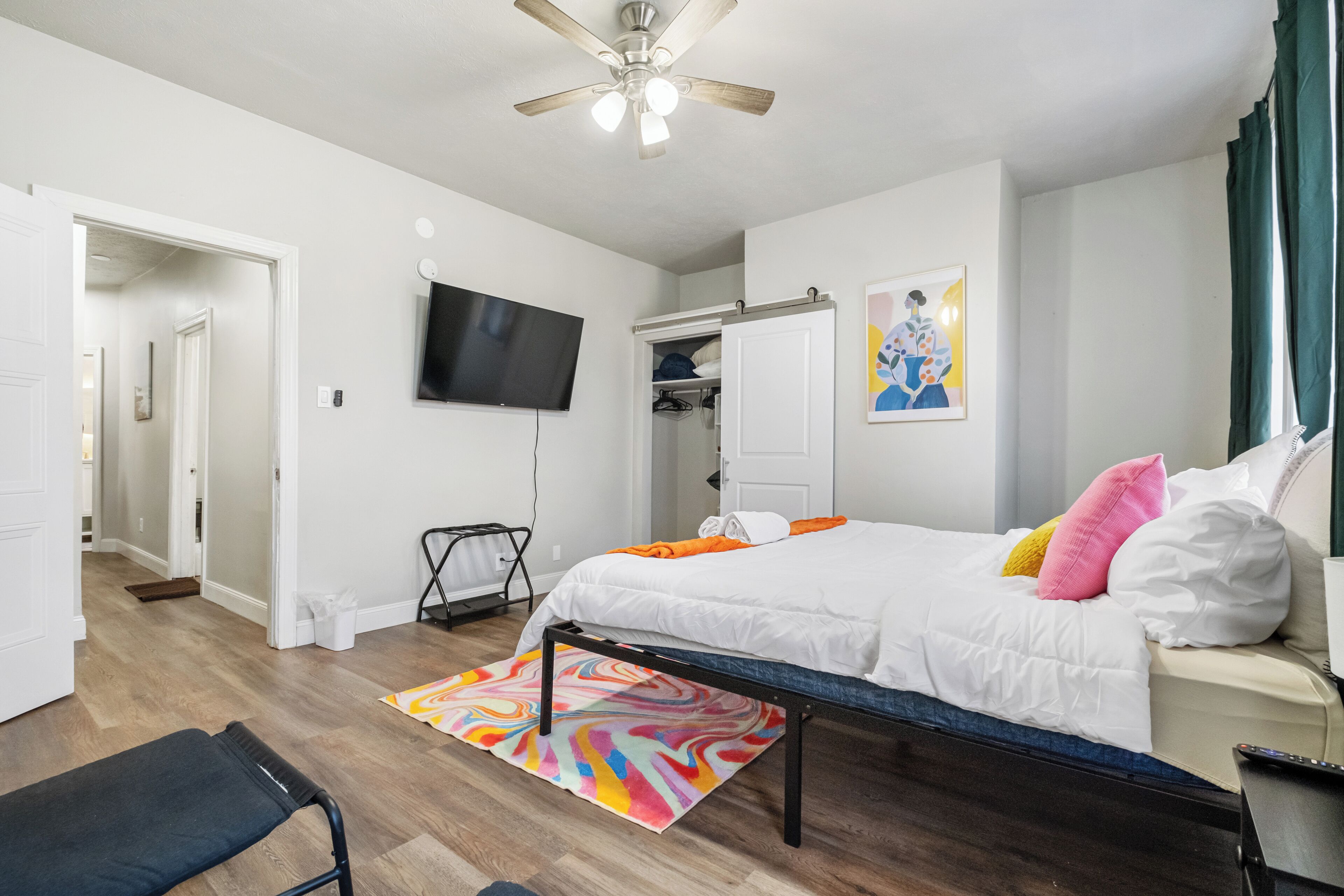 A bedroom with a bed, a ceiling fan, a TV, and a wardrobe.