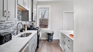 A compact kitchen with grey cabinets, a stainless steel sink, and a view of a wooden deck through a window. - House of Fun-Large Family Home W/HotTub & Games (Pittsburgh)