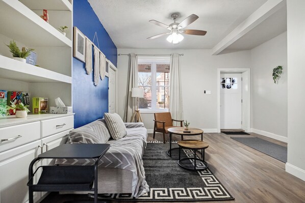 Un salon moderne avec un mur d’accent bleu, un ventilateur de plafond, un canapé, une table basse et une table à manger.