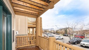 Un balcon en bois offrant une vue sur un parking et, au loin, sur des montagnes enneigées.