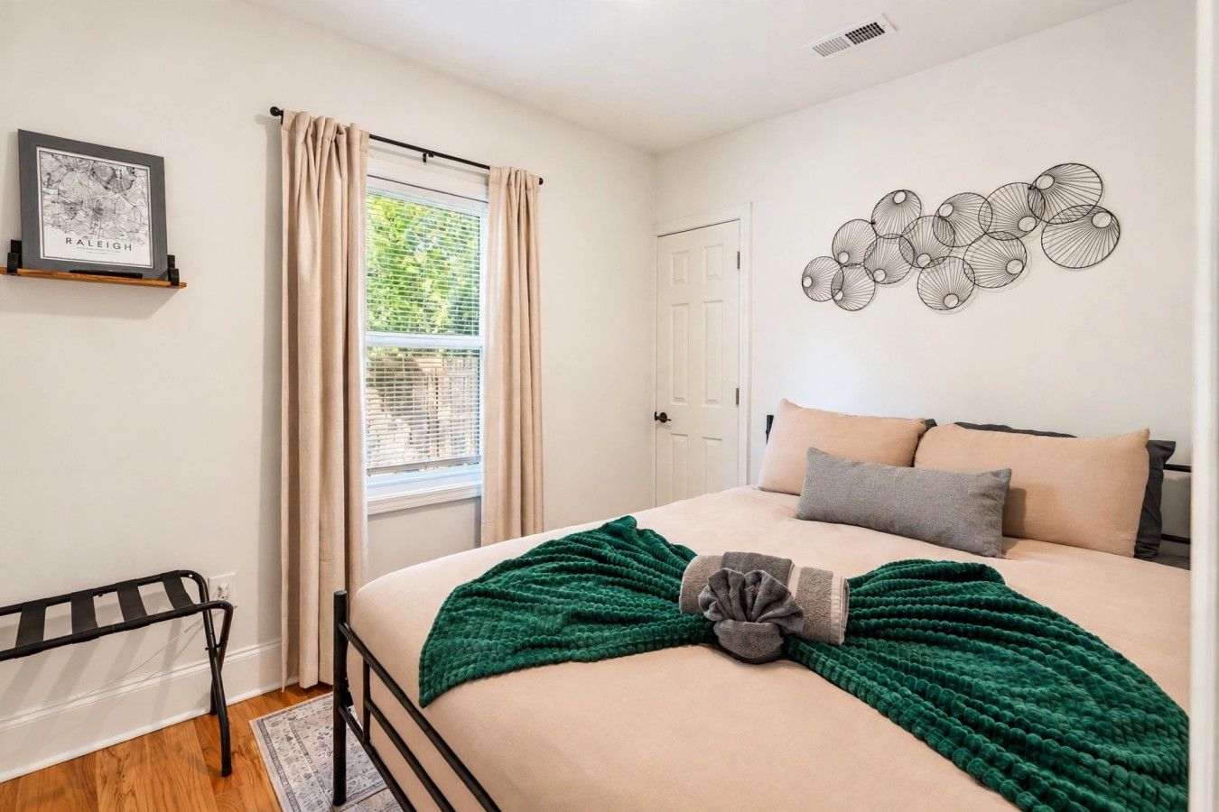 A bedroom with a bed, a window with curtains, a door, a wall-mounted artwork, and a radiator.