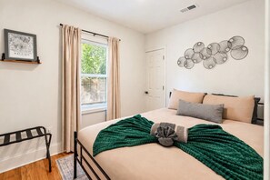 Een slaapkamer met een bed, een raam met gordijnen, een deur, een aan de muur hangend kunstwerk en een radiator.