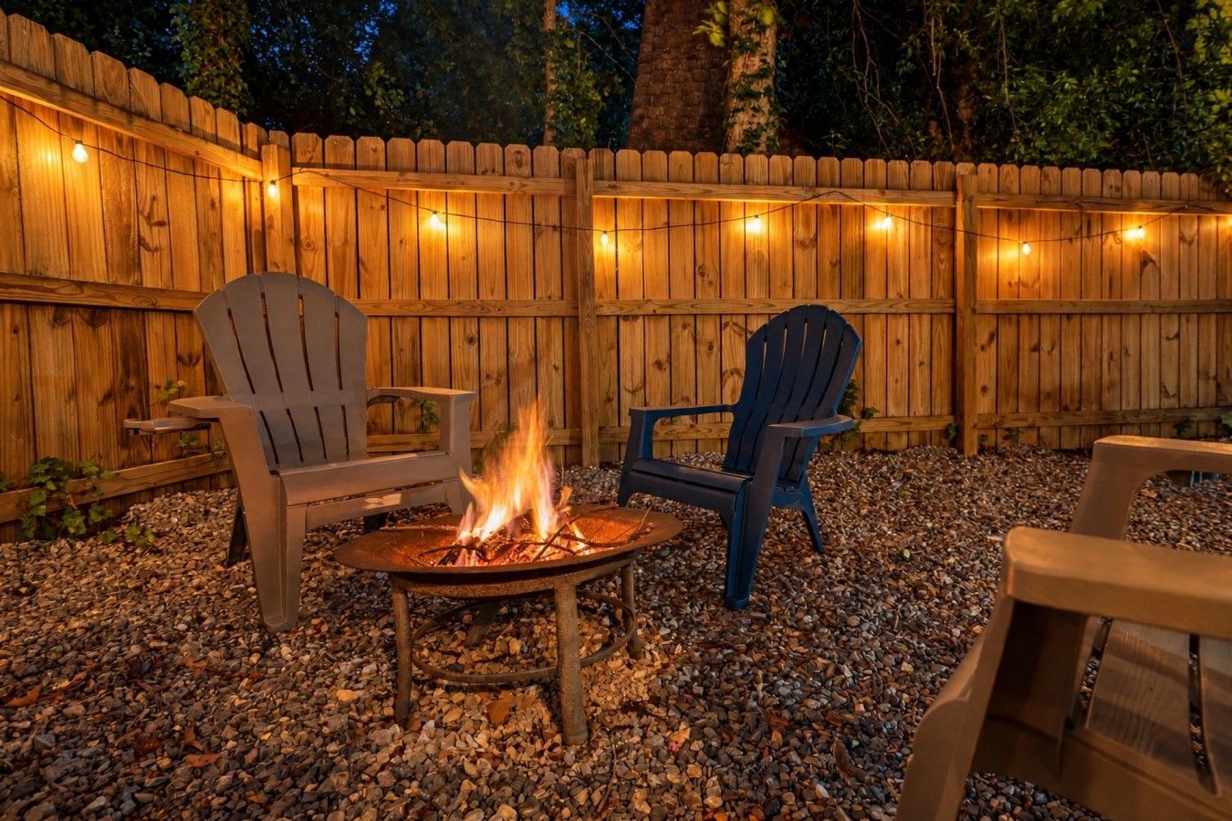 An outdoor seating area with a fire pit, surrounded by wooden chairs and a wooden fence.