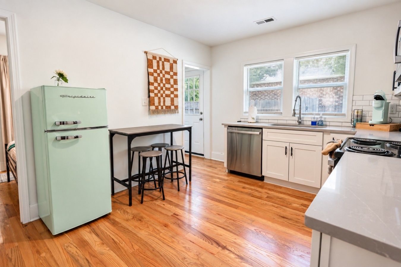 A kitchen with a refrigerator, bar stools, a dishwasher, and a stove.