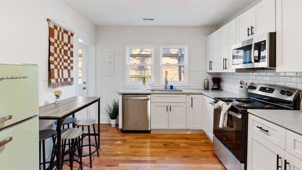 Une cuisine moderne avec des meubles blancs, une cuisinière en acier inoxydable et une décoration murale à carreaux.