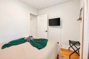 Un dormitorio con una cama, un televisor montado en la pared y una puerta.