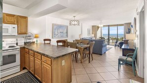 A modern kitchen with wooden cabinets, a built-in microwave, and a dining area with wicker chairs. - Seaside Beach 5417- Two Bedrooms Waterfront Condo With Pool Sauna Amazing Ocean View Balcony (Orange Beach)